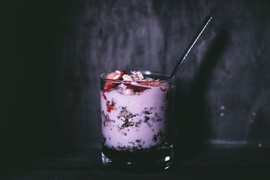 Dark, moody close-up of a delicious yogurt parfait with granola and berries in a glass.