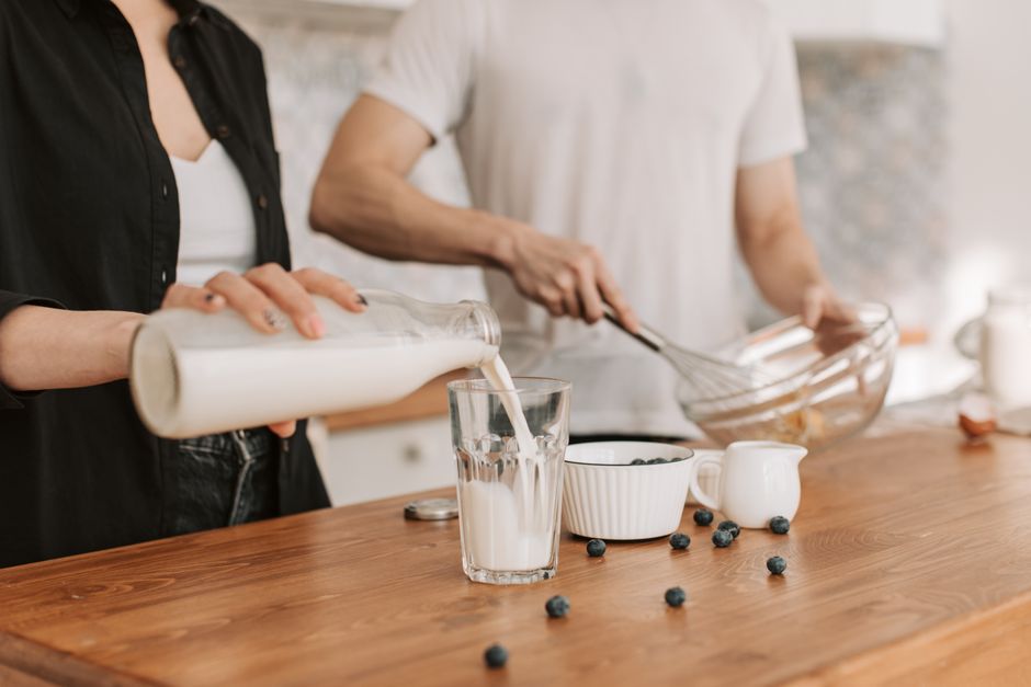 A couple in a kitchen preparing breakfast with milk, blueberries, and cooking utensils.