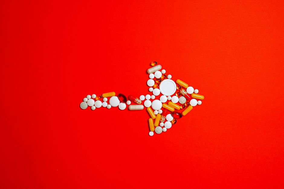 An artistic arrangement of multicolored pills forming an arrow on a vivid red background.