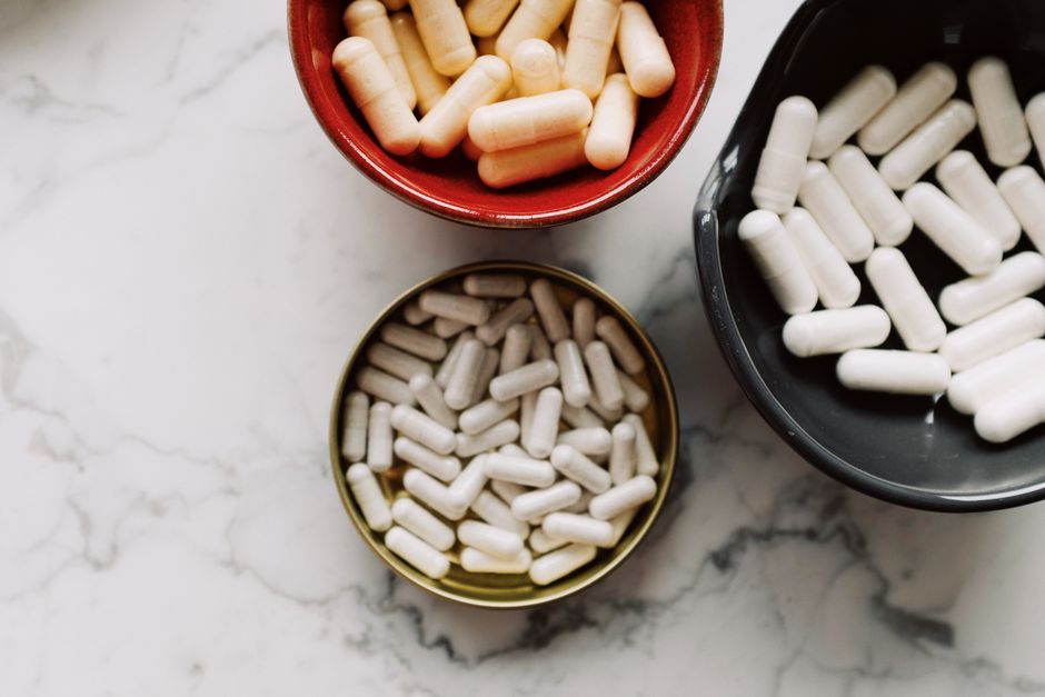 Top view of various capsules in bowls placed on a marble surface, emphasizing healthcare and medication themes.