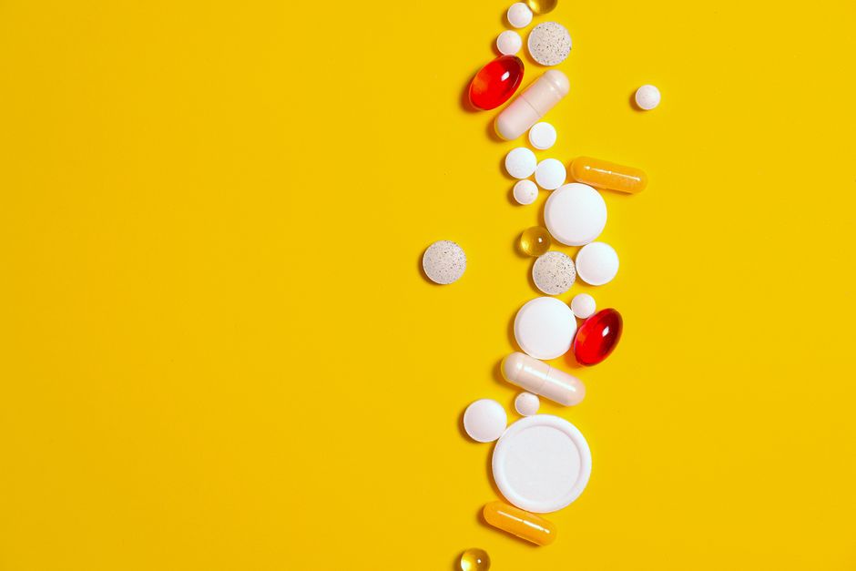 Assorted pills and capsules scattered on a bright yellow background, representing healthcare and medication.