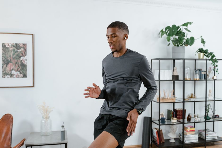 Man working out at home, wearing earbuds, surrounded by modern decor and lush plants.