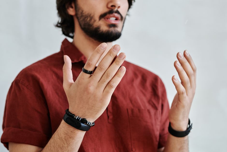 Close-up of a man's hands with bracelets and rings gesturing against a white background.
