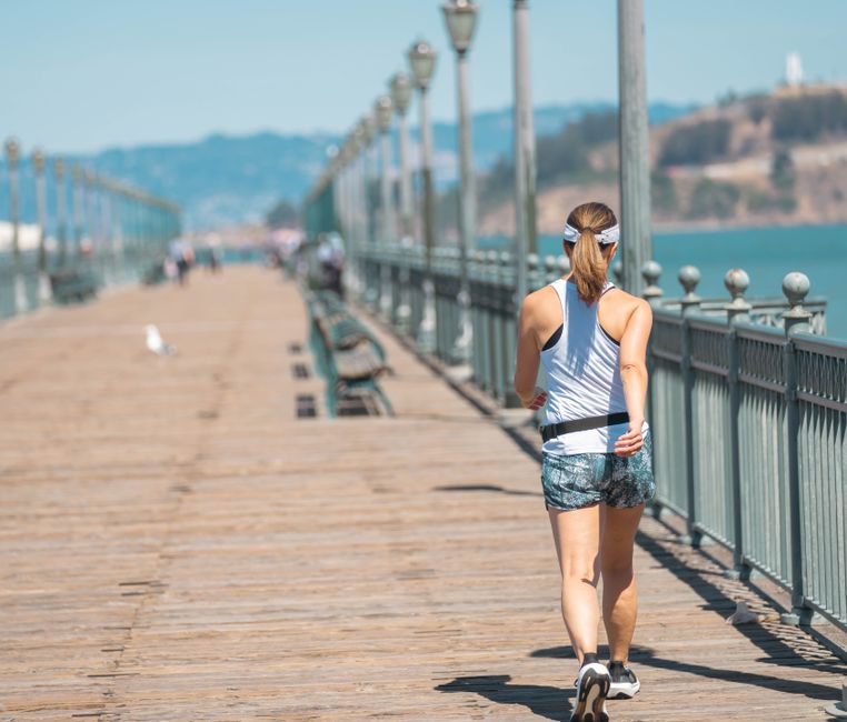 A young woman jogging on a sunny boardwalk by the sea, capturing fitness and leisure.